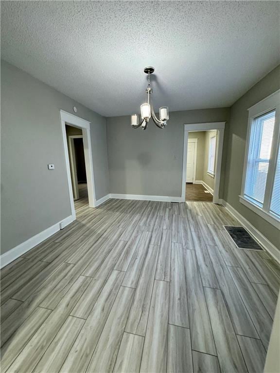 unfurnished dining area with baseboards, an inviting chandelier, a textured ceiling, visible vents, and wood finished floors