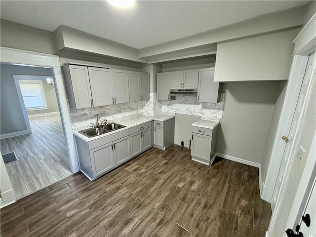 kitchen with under cabinet range hood, a sink, decorative backsplash, gray cabinetry, and dark wood-style floors