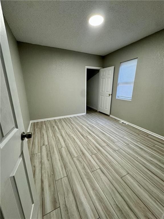 unfurnished bedroom with visible vents, light wood-type flooring, baseboards, and a textured ceiling