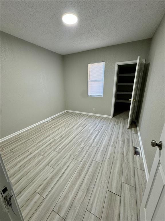unfurnished bedroom featuring light wood-style floors, baseboards, visible vents, and a textured ceiling