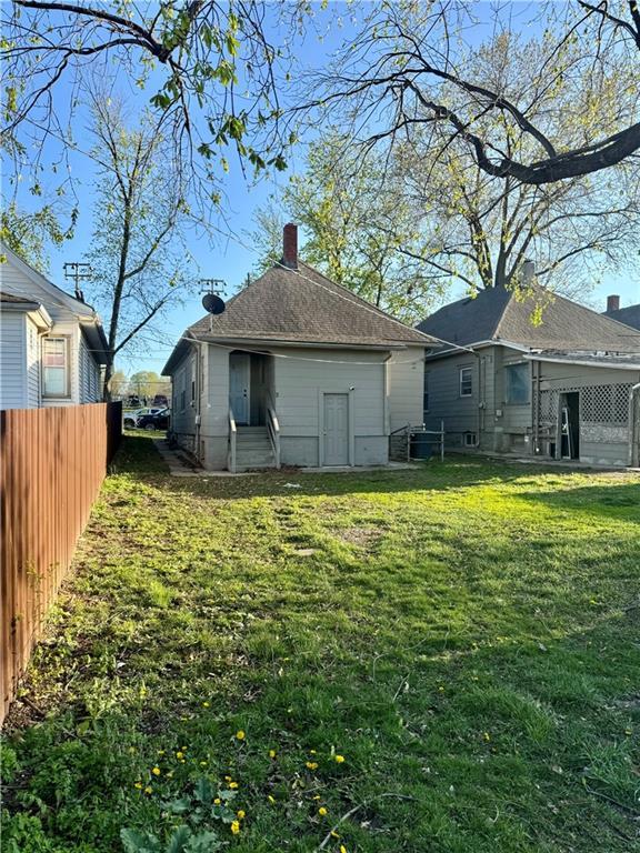 rear view of property featuring a chimney, fence, and a lawn