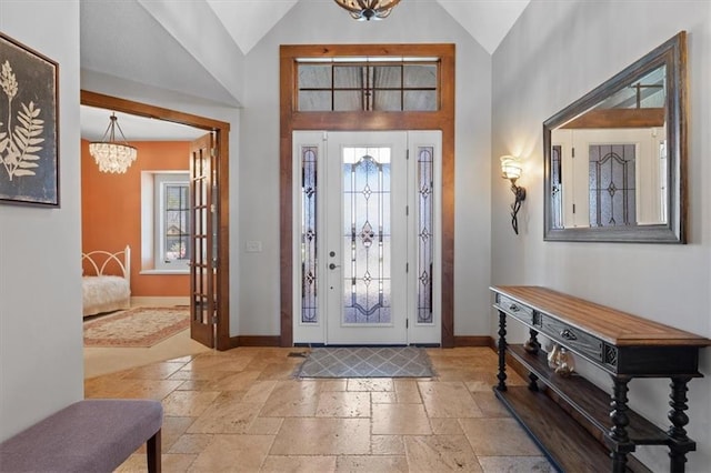 entryway featuring a chandelier, stone tile flooring, baseboards, and high vaulted ceiling