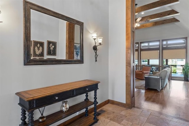 corridor featuring baseboards, beamed ceiling, stone tile flooring, and a high ceiling