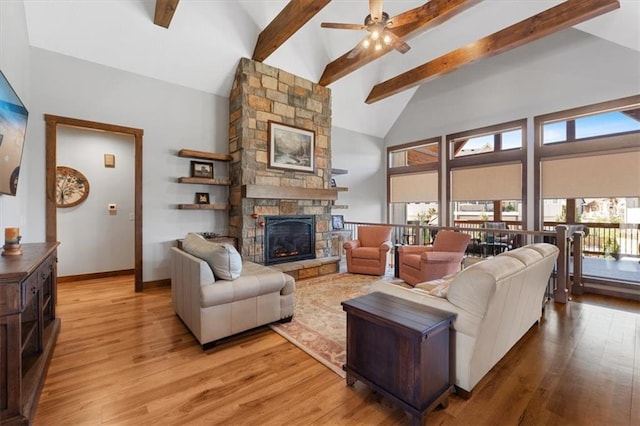 living room with ceiling fan, beamed ceiling, a stone fireplace, wood finished floors, and baseboards