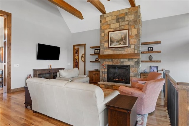 living area with light wood-style floors, beam ceiling, high vaulted ceiling, a stone fireplace, and baseboards