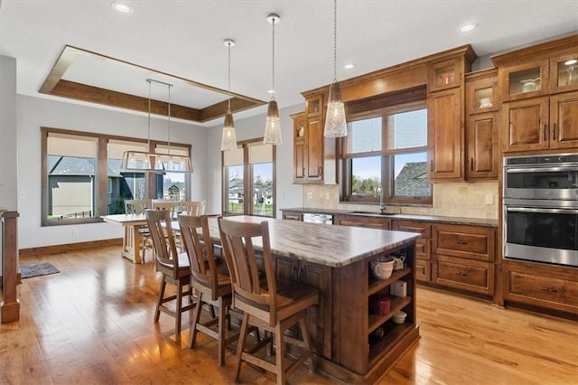 kitchen featuring stainless steel appliances, a sink, a raised ceiling, a center island, and backsplash