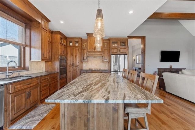 kitchen featuring appliances with stainless steel finishes, a sink, brown cabinetry, backsplash, and recessed lighting