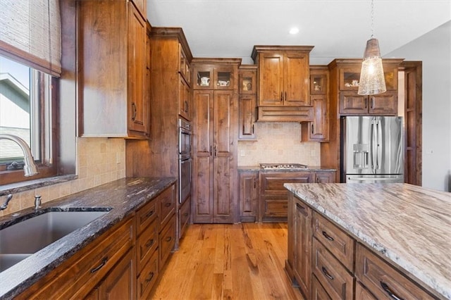 kitchen with stainless steel appliances, a sink, brown cabinets, light wood finished floors, and decorative light fixtures