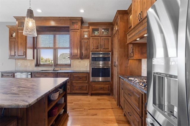kitchen with appliances with stainless steel finishes, a sink, light wood-type flooring, brown cabinets, and decorative backsplash