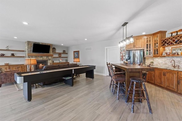 game room with a stone fireplace, light wood-style flooring, recessed lighting, baseboards, and wet bar