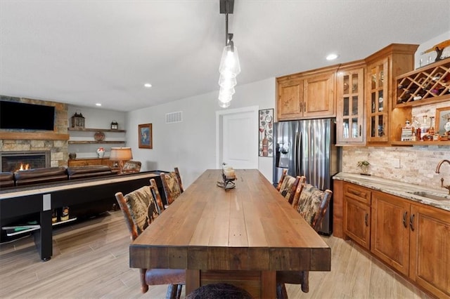 dining room with light wood-type flooring, recessed lighting, and a stone fireplace