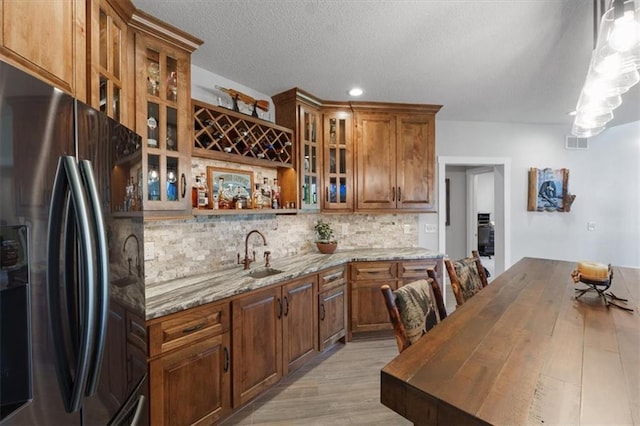 kitchen featuring black refrigerator with ice dispenser, a sink, backsplash, light stone counters, and light wood-type flooring