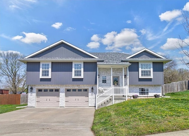 split foyer home featuring a garage, fence, stone siding, a front lawn, and driveway