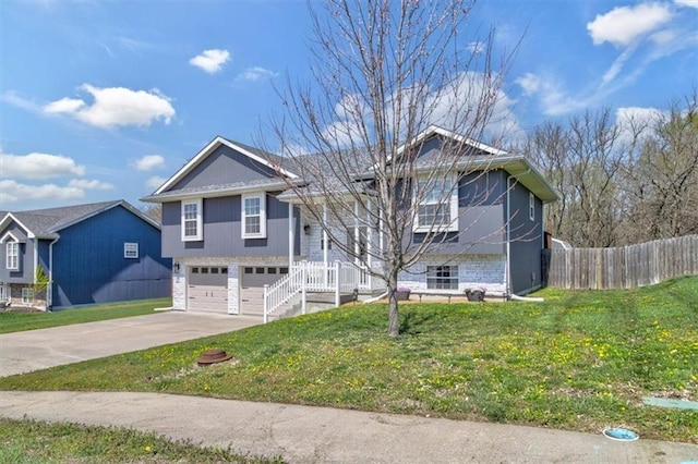 split foyer home featuring concrete driveway, stone siding, an attached garage, a front yard, and fence