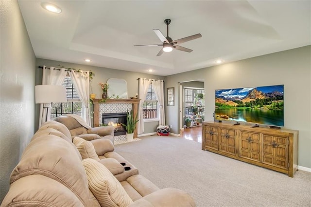 carpeted living room featuring baseboards, recessed lighting, a ceiling fan, a tray ceiling, and a tile fireplace