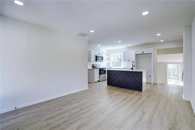 kitchen featuring stainless steel appliances, a wealth of natural light, light wood finished floors, and baseboards