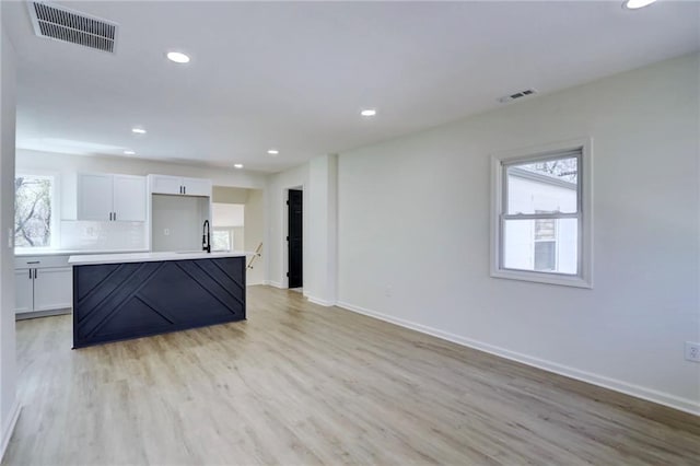 kitchen with light wood finished floors, baseboards, white cabinetry, and visible vents
