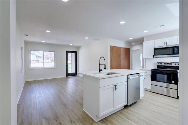 kitchen with light wood-type flooring, appliances with stainless steel finishes, a sink, and white cabinetry