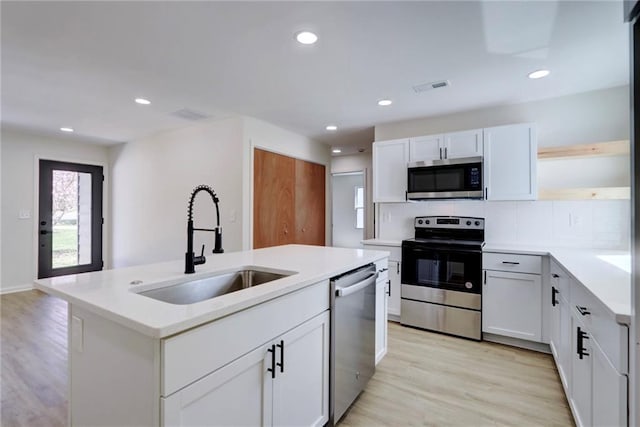 kitchen with an island with sink, light wood-style flooring, visible vents, stainless steel appliances, and a sink
