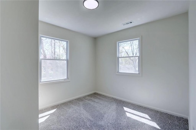 carpeted spare room with a healthy amount of sunlight, baseboards, and visible vents