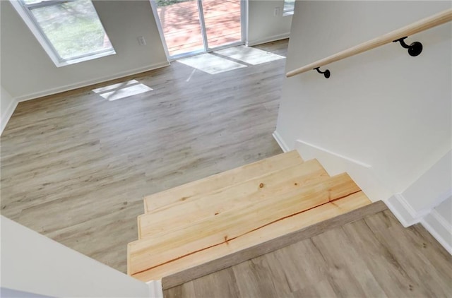 staircase featuring baseboards, wood finished floors, and a healthy amount of sunlight
