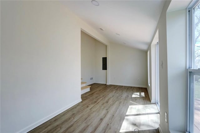 unfurnished room with electric panel, light wood finished floors, baseboards, and vaulted ceiling