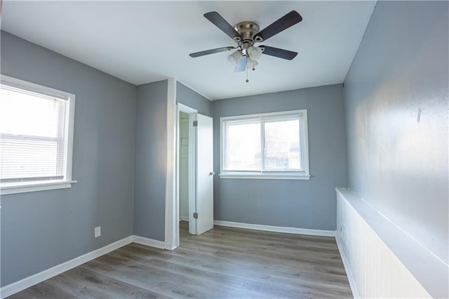 9904 E 60th Ter, Raytown, MO 64133 - unfurnished bedroom with ceiling fan, multiple windows, baseboards, and wood finished floors