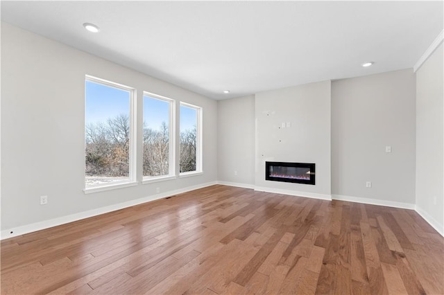 unfurnished living room with baseboards, recessed lighting, a glass covered fireplace, and wood finished floors