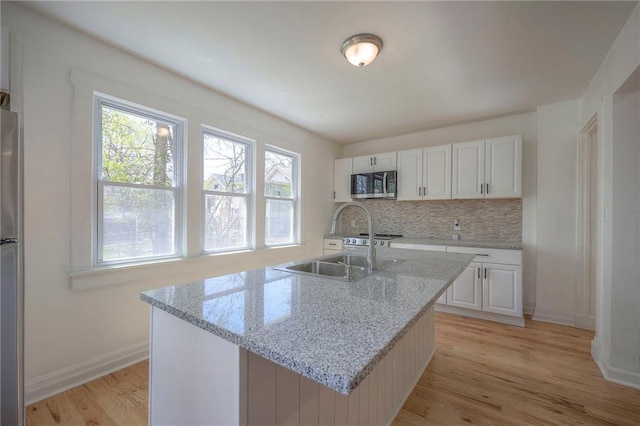 1607 E 37th St, Kansas City, MO 64109 - kitchen with stainless steel microwave, light wood finished floors, decorative backsplash, white cabinetry, and a sink