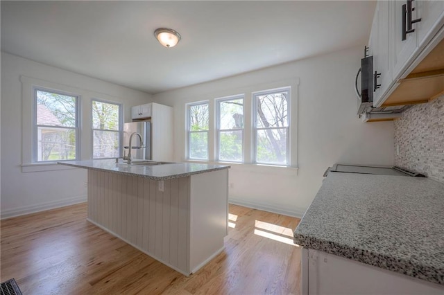 1607 E 37th St, Kansas City, MO 64109 - kitchen with white cabinetry, light wood finished floors, stainless steel appliances, light stone countertops, and an island with sink