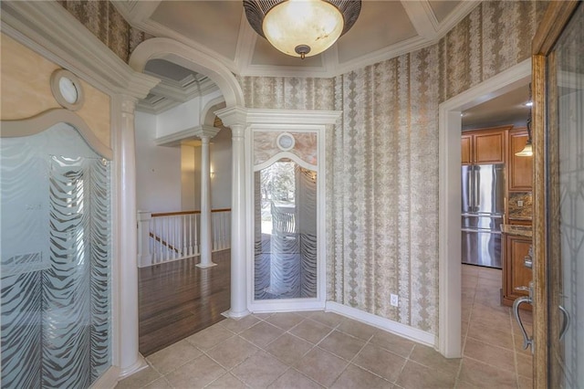 hallway featuring baseboards, wallpapered walls, light tile patterned floors, crown molding, and decorative columns