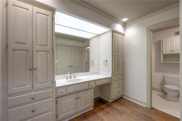 bathroom with vanity, baseboards, ornamental molding, toilet, and wood finished floors