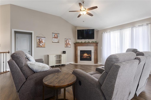 living area with baseboards, vaulted ceiling, a warm lit fireplace, dark wood-style floors, and ceiling fan