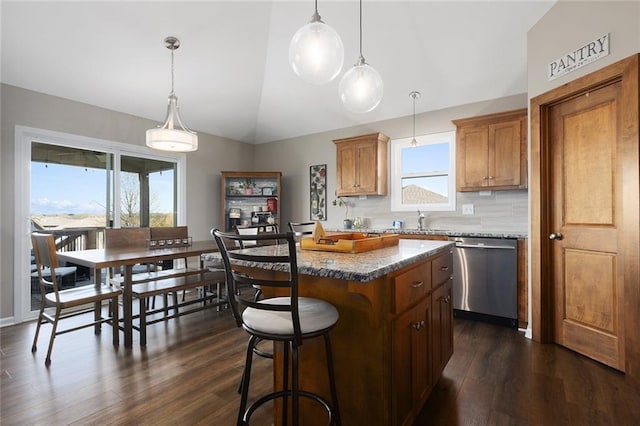 kitchen featuring dark wood-type flooring, vaulted ceiling, a center island, dishwasher, and a breakfast bar area