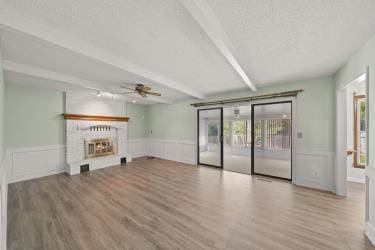 11930 Charlotte St, Kansas City, MO 64146 - unfurnished living room with ceiling fan, beam ceiling, wood finished floors, a wainscoted wall, and a lit fireplace