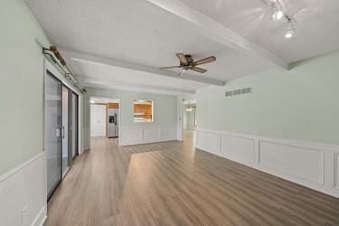 11930 Charlotte St, Kansas City, MO 64146 - unfurnished living room with beamed ceiling, light wood finished floors, ceiling fan, a wainscoted wall, and a decorative wall