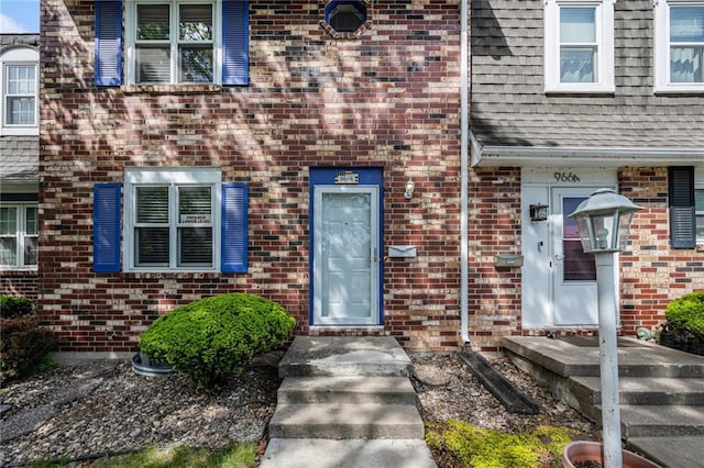 property entrance featuring brick siding and a shingled roof