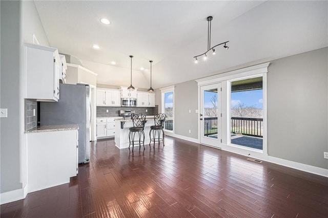kitchen with tasteful backsplash, white cabinets, baseboards, appliances with stainless steel finishes, and a kitchen bar