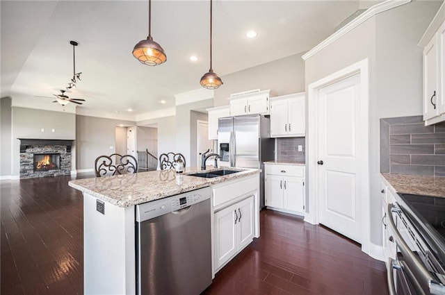 kitchen with a sink, ceiling fan, appliances with stainless steel finishes, a fireplace, and backsplash