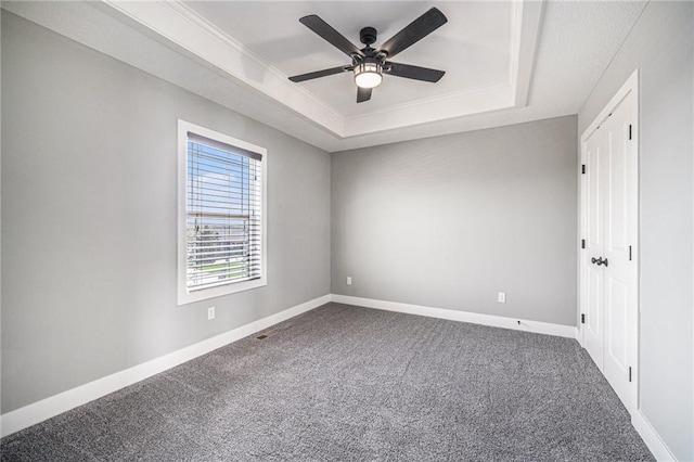 unfurnished bedroom with baseboards, ornamental molding, a ceiling fan, a tray ceiling, and carpet