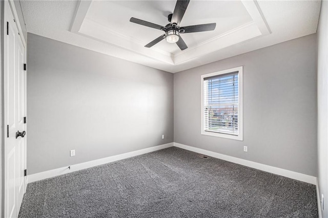 carpeted empty room with ceiling fan, a raised ceiling, and baseboards