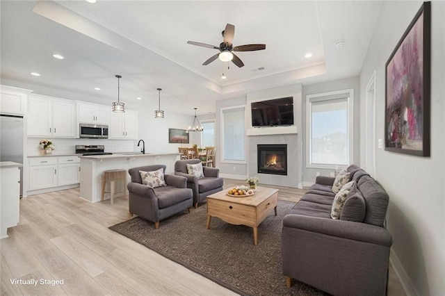 19703 W 196th St, Spring Hill, KS 66083 - living room featuring a tray ceiling, light wood finished floors, recessed lighting, a ceiling fan, and a glass covered fireplace
