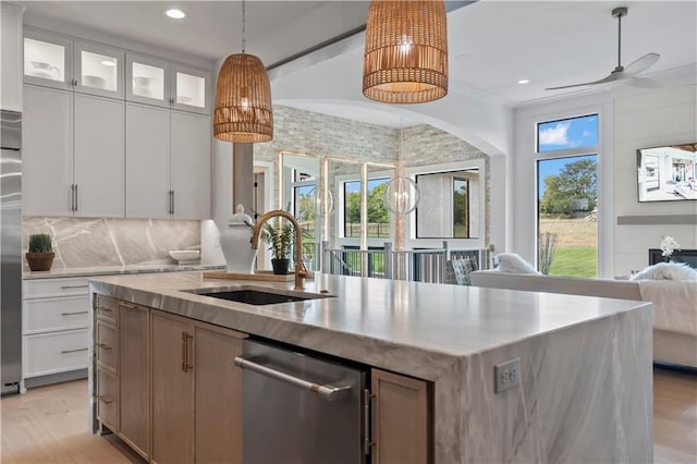 kitchen featuring open floor plan, a center island with sink, stainless steel dishwasher, light wood finished floors, and a sink