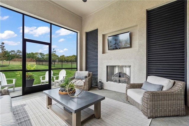 living room with a textured wall, a wealth of natural light, a glass covered fireplace, and crown molding