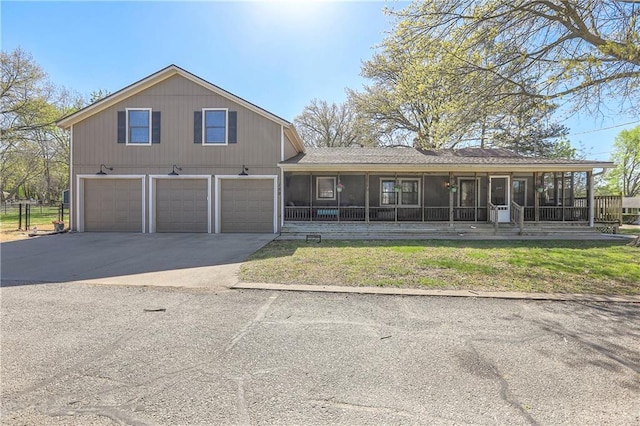 view of front of home featuring an attached garage, a sunroom, driveway, and a front lawn