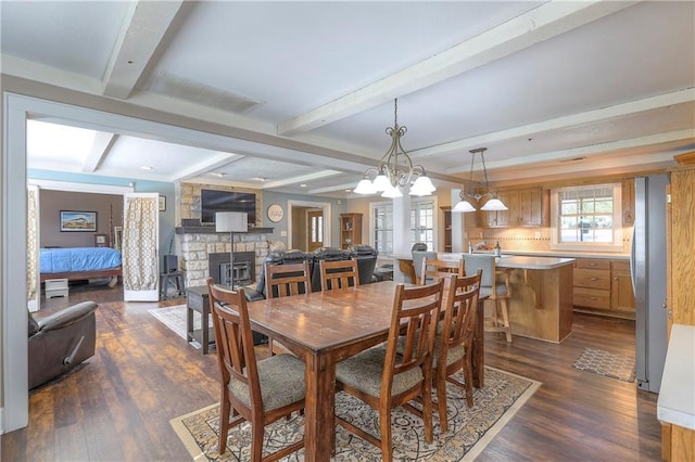 dining space featuring dark wood-type flooring, beamed ceiling, a chandelier, and a fireplace
