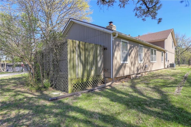 view of side of property with a yard, central air condition unit, and a chimney