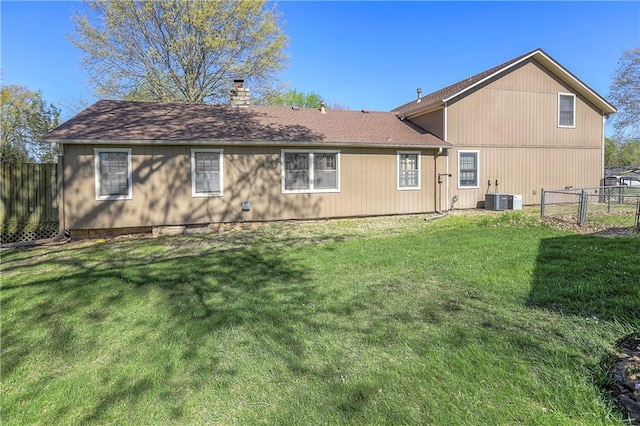 rear view of property with cooling unit, a chimney, fence, and a lawn