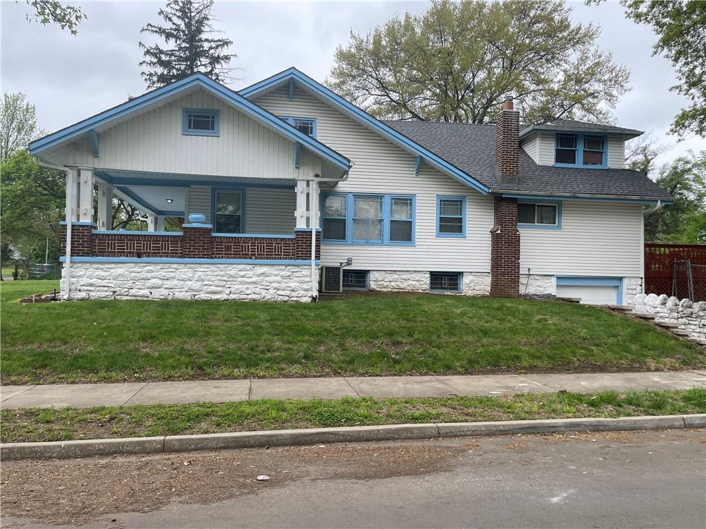 view of front facade with roof with shingles, an attached garage, a front lawn, a porch, and a chimney