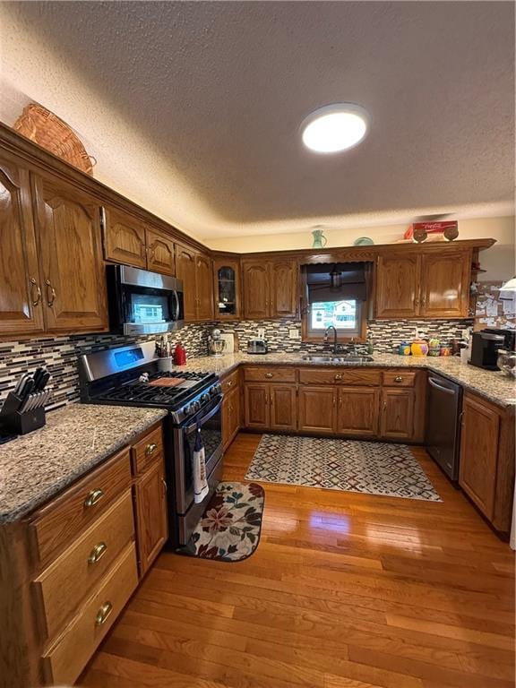 1200 Susan St, Kearney, MO 64060 - kitchen featuring appliances with stainless steel finishes, a sink, light wood finished floors, decorative backsplash, and a textured ceiling
